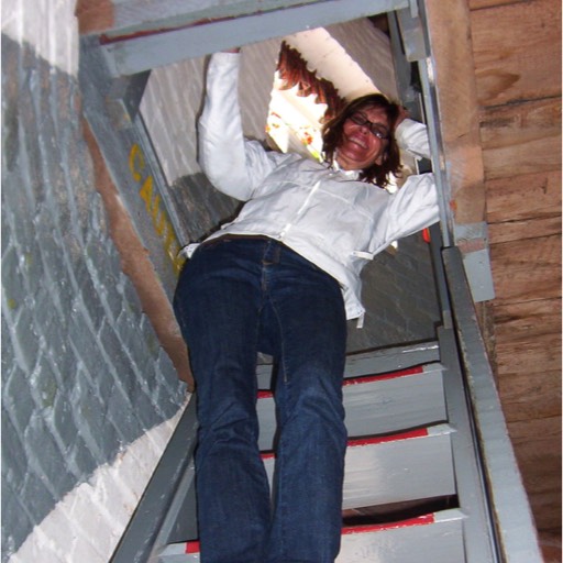 Shot looking up the narrow staircase at the lighthouse with Julie coming down. She is holding her neck. 