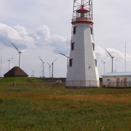 White lighthouse in the foreground, with fans from a wind farm in the background. 