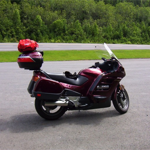 Photo of a red Honda ST 1100 motorcycle by the side of the road, with a pair of glove sitting on the driver's seat. 