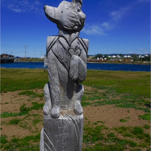 Sculpture of a dog sitting on its haunches, with its left paw raised, looking off to its right. 