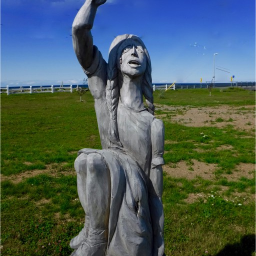 Sculpture of a girl or woman, hair braided, looking up and reaching up with her right arm. 