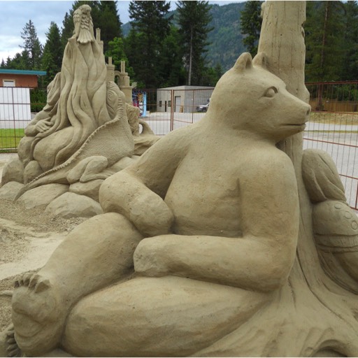 Sand sculpture of a seated bear leaning against a tree trunk, looking back over his/her shoulder to what's behind the tree. 