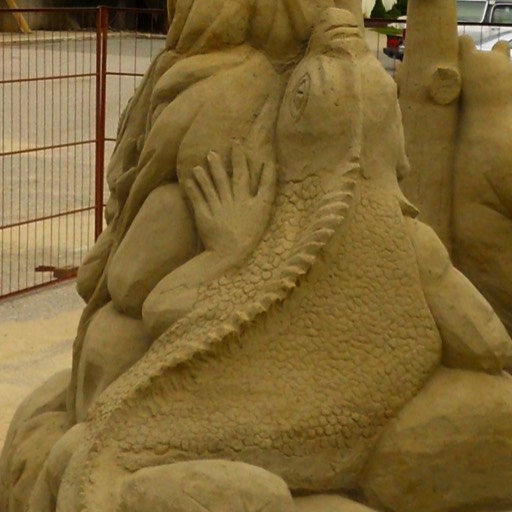 Sand sculpture of a lizard climbing up a tree to its prey at the top, a sleeping bird. 