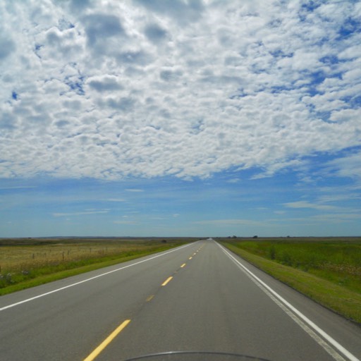 Photo of two-lane highway on the prairie streching into the distance on the flat prairie. 