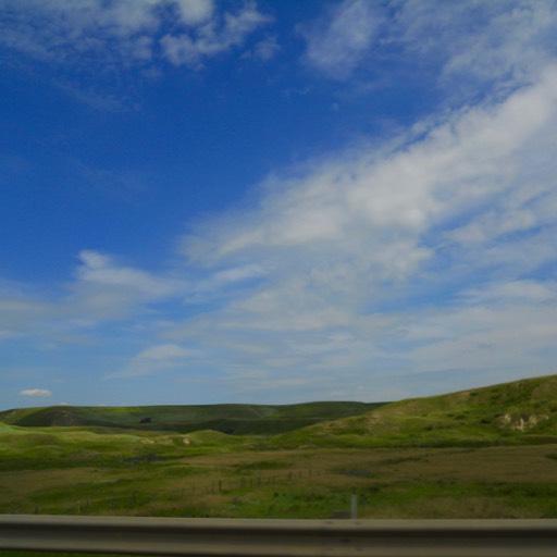 Photo of the prairie and the sky. Instead of being flat, the prairie rises to a couple of small hills in the distance.